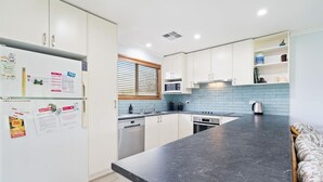 Una cocina moderna con armarios blancos, encimera negra y una ventana con persianas.