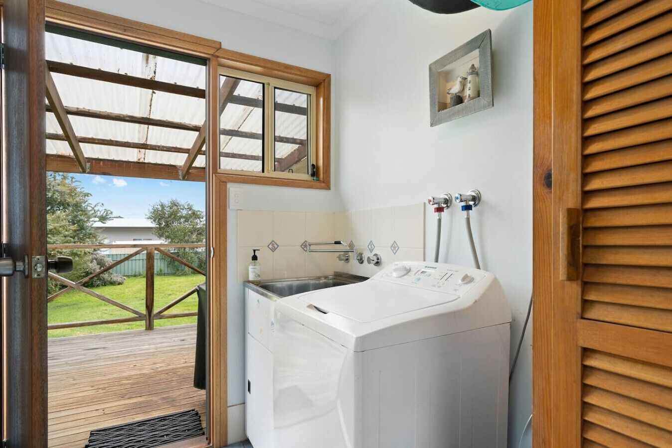A laundry room with a washing machine, a sink, and a window overlooking a deck.