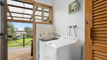 A laundry room with a washing machine, a sink, and a window overlooking a deck.