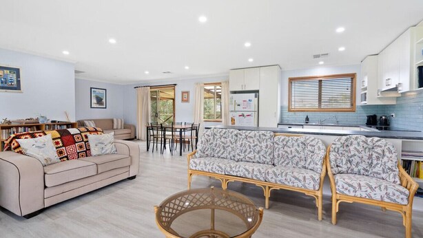 Una sala de estar moderna con un sofá, una mesa de comedor y una zona de cocina con armarios y una ventana.