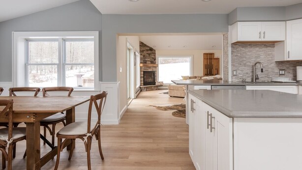 A spacious kitchen with a large island, wooden dining table, and chairs. There is a stone fireplace and a view of a living area with a sofa and a rug. - Ski Mountain Chalet w/ Hot tub, Fireplace, Game Room -Windham Mountain (Hensonville)
