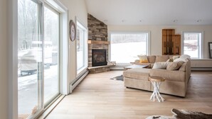 A spacious living room with a fireplace, large windows, and a cozy seating area. - Ski Mountain Chalet w/ Hot tub, Fireplace, Game Room -Windham Mountain (Hensonville)
