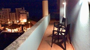 Un balcon avec deux chaises et une table, donnant sur une vue panoramique de la ville la nuit.