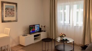 Un salon moderne avec un téléviseur à écran plat, un canapé blanc, une table basse en verre et un tableau encadré accroché au mur.
