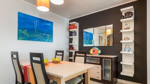 A dining area with a wooden table, chairs, and a painting of a sailboat. There are shelves with decorative items and a mirror on the wall. - HC Torreira Beach (Torreira Aveiro)