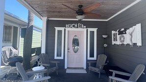 A covered porch with a ceiling fan, a white door with a frosted glass window, and two Adirondack chairs.
