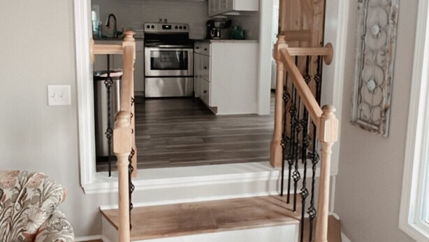 A staircase with wooden railings leading to a kitchen area with white cabinets and stainless steel appliances.