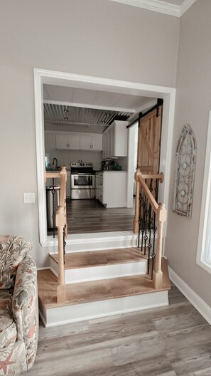 Una escalera con barandillas de madera que lleva a una zona de cocina con armarios blancos y electrodomésticos de acero inoxidable.