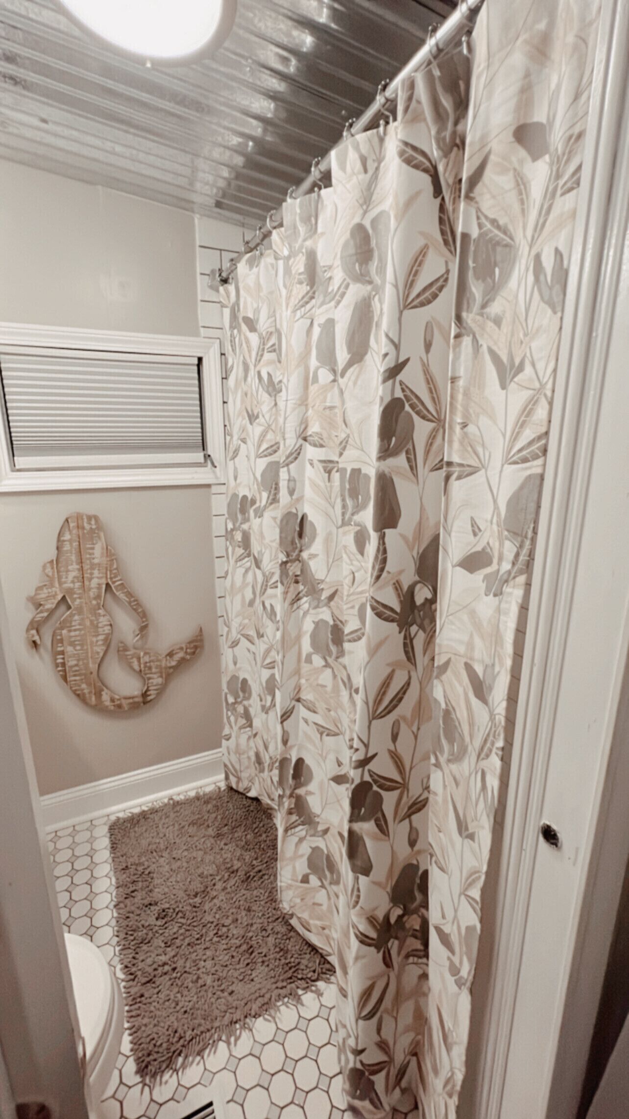 Ein Badezimmer mit Duschvorhang mit Blumenmuster, einem hexagonal gemusterten Teppich und einem an der Wand befestigten dekorativen Gegenstand, der eine Schlange darstellt.