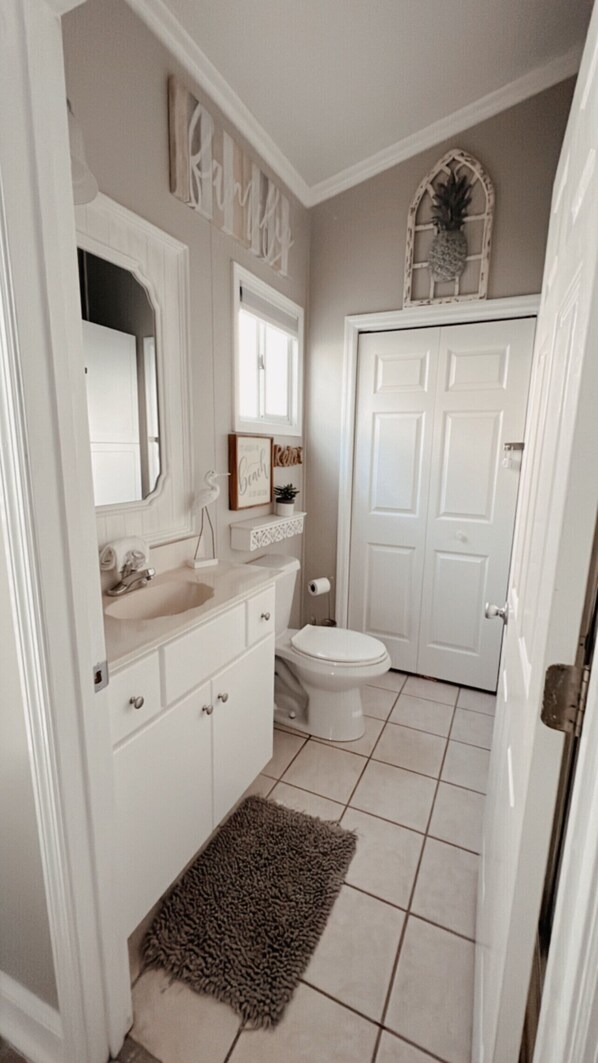 A bathroom with a white vanity, a toilet, and a door with a decorative mirror above it.