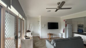 A living room with a grey sofa, a television mounted on the wall, and a ceiling fan.
