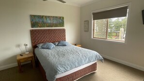Une chambre à coucher comprenant un lit, une table de chevet, une lampe, une fenêtre avec vue et un ventilateur de plafond.