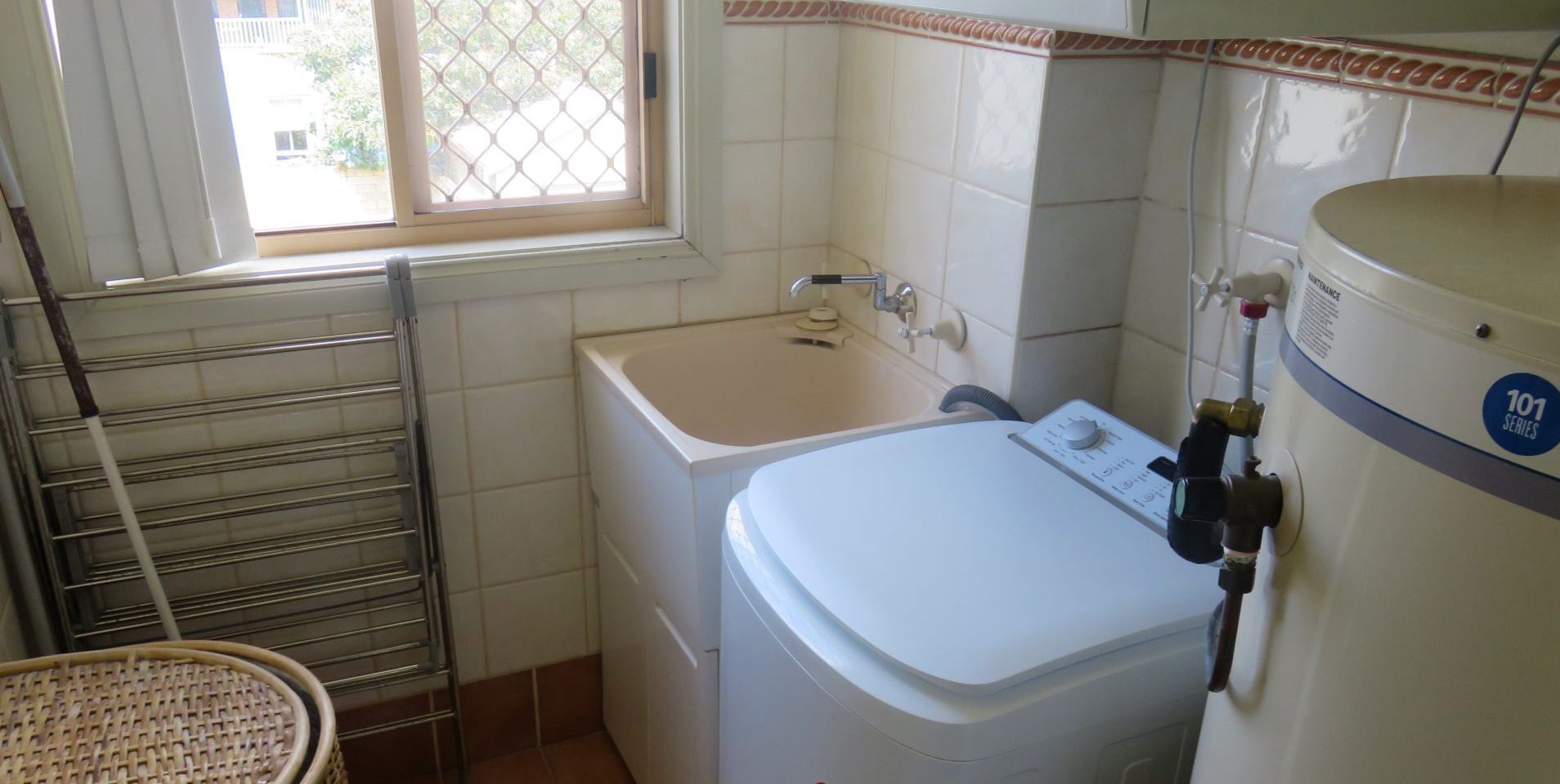 A compact laundry room with a washing machine, a sink, and a drying rack.