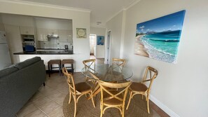 A compact living space with a dining area, kitchenette, and a beach-themed painting.