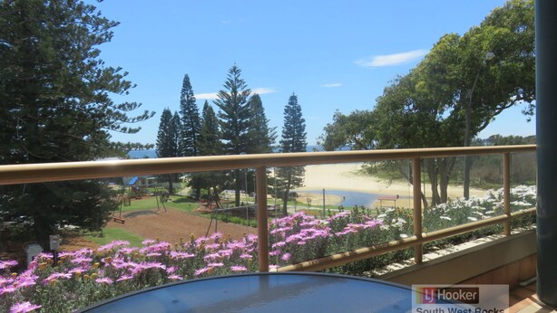 A balcony with a view of a beach, trees, and a playground.