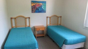 A room with two single beds, a small wooden nightstand, a painting on the wall, and a window on the right. - POINT BRINER UNIT 3 - THREE BEDROOM WITH MAIN BEACH VIEWS (South West Rocks)