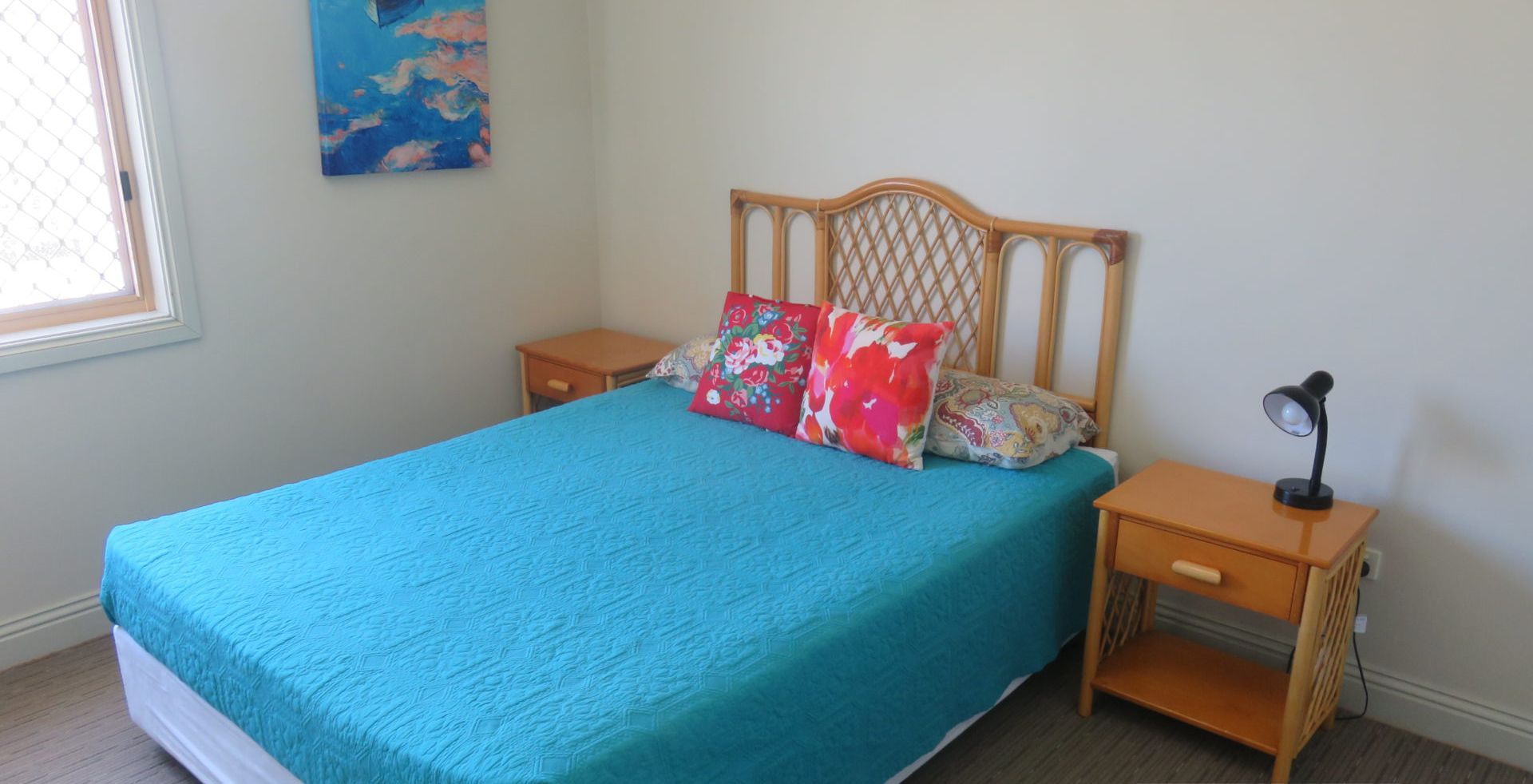 A bedroom with a bed, two nightstands, a lamp, and a painting on the wall.