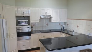 A compact kitchen with white cabinets, a built-in oven, a microwave, a stainless steel range hood, and a black countertop.
