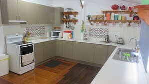 Una cucina compatta con piano cottura, microonde e lavello. Si notano mobili in legno e un piccolo ripiano con utensili da cucina.