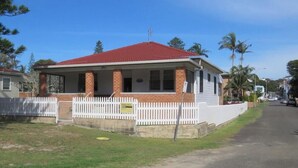 A two-story house with a red roof, a white picket fence, and a driveway. - MRS MOTTEES COTTAGE - SHORT STROLL TO BEACH, AIRCONDITIONED & PET FRIENDLY. (South West Rocks)