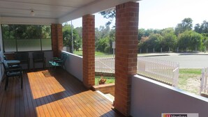 A covered outdoor area with wooden flooring, brick pillars, and a white fence. - MRS MOTTEES COTTAGE - SHORT STROLL TO BEACH, AIRCONDITIONED & PET FRIENDLY. (South West Rocks)
