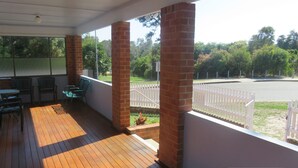 A covered outdoor area with wooden flooring, brick pillars, and a white fence. - MRS MOTTEES COTTAGE - SHORT STROLL TO BEACH, AIRCONDITIONED & PET FRIENDLY. (South West Rocks)