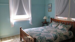 A bedroom with a bed, a nightstand, a lamp, and a window with curtains. - MRS MOTTEES COTTAGE - SHORT STROLL TO BEACH, AIRCONDITIONED & PET FRIENDLY. (South West Rocks)