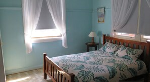 A bedroom with a bed, a nightstand, a lamp, and a window with curtains. - MRS MOTTEES COTTAGE - SHORT STROLL TO BEACH, AIRCONDITIONED & PET FRIENDLY. (South West Rocks)