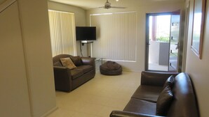 A living room with a brown leather sofa, a brown bean bag, and a television on a stand. - REFLECTIONS UNIT 1 - AIRCONDITIONING & THREE BEDROOMS (South West Rocks)
