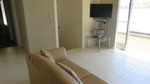 A living room with a beige sofa, a glass coffee table, a flat-screen TV, and a sliding glass door leading to an outdoor area. - REFLECTIONS UNIT 1 - AIRCONDITIONING & THREE BEDROOMS (South West Rocks)