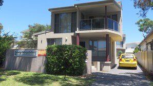 A two-story building with a balcony, a sign for 'Reflections Holiday Lettings', and a yellow taxi parked in front. - REFLECTIONS UNIT 1 - AIRCONDITIONING & THREE BEDROOMS (South West Rocks)