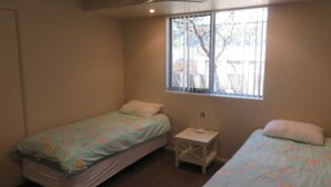 A small, cozy bedroom with two single beds, a small bedside table, and a window with blinds. - REFLECTIONS UNIT 1 - AIRCONDITIONING & THREE BEDROOMS (South West Rocks)