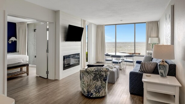 Een moderne hotelkamer met een groot raam met uitzicht op zee, een flatscreen televisie aan de muur, een bank, een kleine tafel en een bankje.