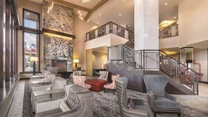 A spacious lobby with a stone fireplace, multiple seating areas, and a staircase leading to an upper level.