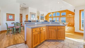A spacious kitchen with wooden cabinets, a large island, and a dining area with green chairs. - Oceanfront Home w/ Private Pool, Hot Tub, Elevator, Game Room, Home Theater (Frisco)