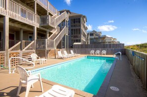 A swimming pool with lounge chairs and a wooden deck, surrounded by a wooden fence and a building with multiple balconies. - Oceanfront Home w/ Private Pool, Hot Tub, Elevator, Game Room, Home Theater (Frisco)