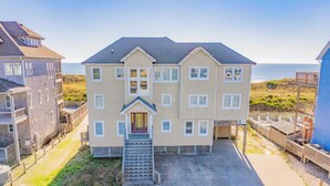 A multi-story building with a central entrance, a staircase leading to the entrance, and a view of the beach in the background. - Oceanfront Home w/ Private Pool, Hot Tub, Elevator, Game Room, Home Theater (Frisco)
