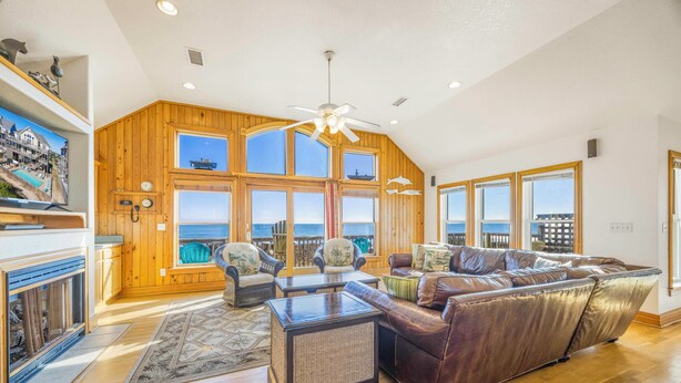 A spacious living room with a large brown leather sofa, wooden walls, and large windows offering a view of the sea. - Oceanfront Home w/ Private Pool, Hot Tub, Elevator, Game Room, Home Theater (Frisco)