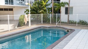 Ein Swimmingpool mit weißem Zaun, umgeben von einem Gebäude mit Balkon und Palmen.