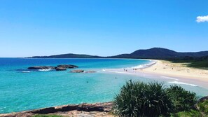 Ein Küstenstrand mit klarem türkisblauem Wasser, einem Sandstrand und einem gebirgigen Hintergrund.