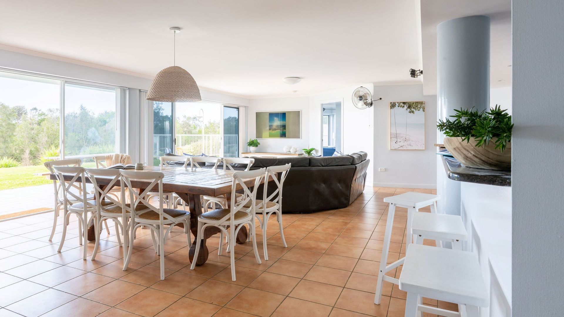 A spacious living area with a dining table, chairs, a sofa, and a large window offering a view of the outdoors.