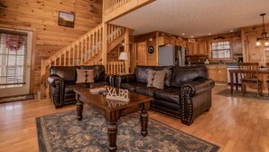 A spacious living area with a wooden staircase, leather sofas, and a kitchen in the background. - ⛰️A Bird Song: Spectacular Views | Minutes from Pigeon Forge & Gatlinburg🌲 (Sevierville)