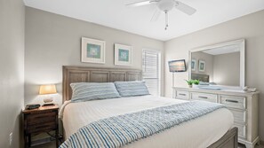 Una camera da letto con un letto, comodino, lampada, televisore, cassettiera e ventilatore a soffitto.