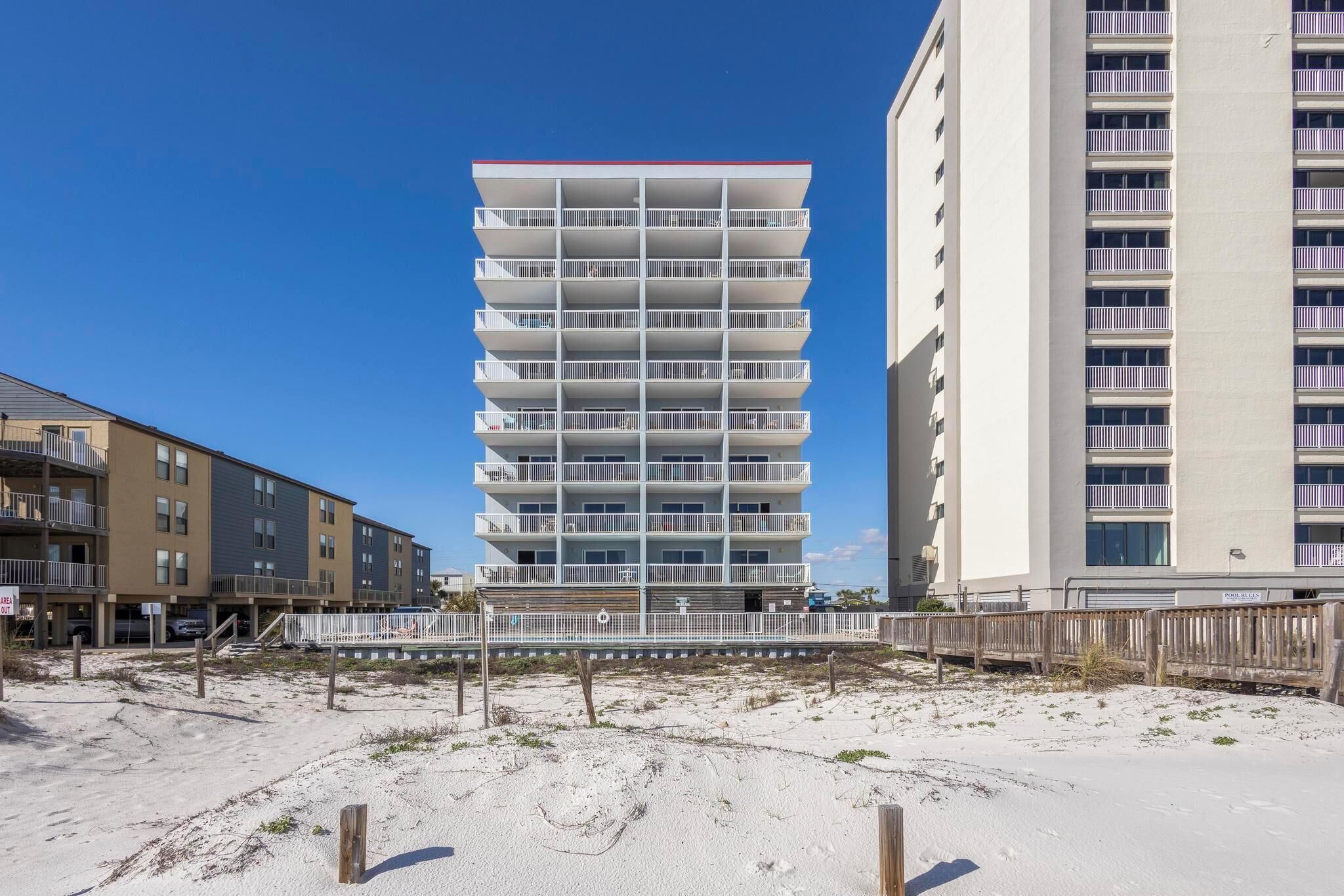 A multi-story hotel with balconies, located near a sandy beach.