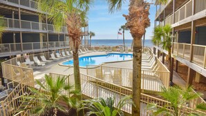 A pool area with lounge chairs and palm trees, surrounded by multi-story buildings with balconies.