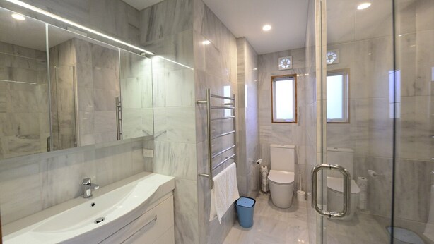 Een moderne badkamer met een glazen douchecabine, een grote spiegel en een witte wastafel.