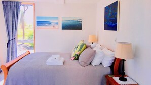 A bedroom with a bed, two wall-mounted lamps, a wooden nightstand, and a window with curtains. - Cockle Lane Beach Studio Two - a beachside getaway, just for you (Waimairi Beach)
