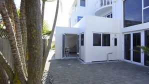 A modern two-story building with a patio area, large windows, and a balcony. - Cockle Lane Beach Studio Two - a beachside getaway, just for you (Waimairi Beach)