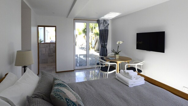 A hotel room with a bed, a desk, a chair, a TV, and a view of the outside. - Cockle Lane Beach Studio Two - a beachside getaway, just for you (Waimairi Beach)