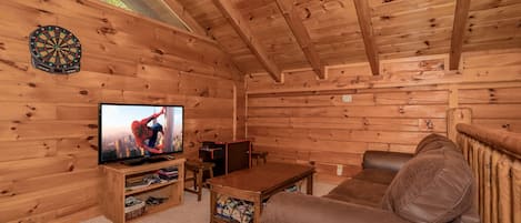 L’intérieur d’un chalet en bois chaleureux et accueillant, avec un téléviseur, un canapé et un jeu de fléchettes.